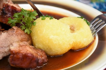 dumplings with fried meat, gravy and fresh parsley on a white plate with a knife and fork