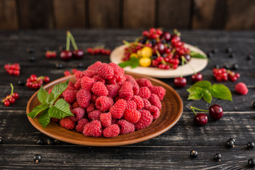 Raspberry, cherry, red currant, blackcurrant on a wooden plate against a dark background. It can be used as a background