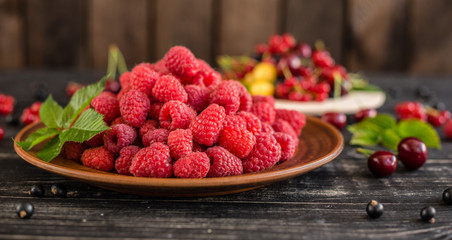 Raspberry, cherry, red currant, blackcurrant on a wooden plate against a dark background. It can be used as a background