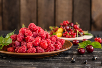 Raspberry, cherry, red currant, blackcurrant on a wooden plate against a dark background. It can be used as a background