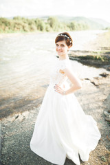 Fototapeta na wymiar Gorgeous beautiful bride smiles while posing by the river with bouquet