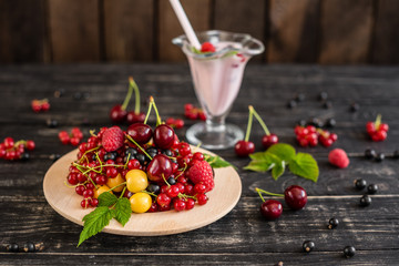 Raspberry, cherry, red currant, blackcurrant on a wooden plate against a dark background. It can be used as a background