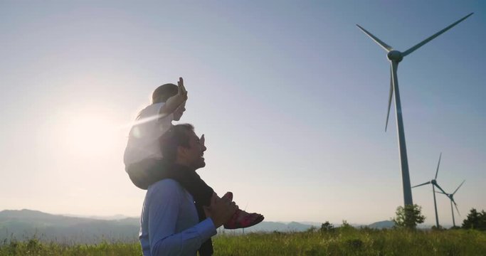 A father engineer holds his daughter in his arms and runs between the wind turbines with great freedom. Concept of: environmental engineering, renewable energy and love for nature and for the family