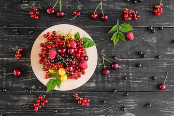 Raspberry, cherry, red currant, blackcurrant on a wooden plate against a dark background. It can be used as a background