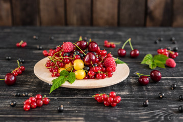 Raspberry, cherry, red currant, blackcurrant on a wooden plate against a dark background. It can be used as a background