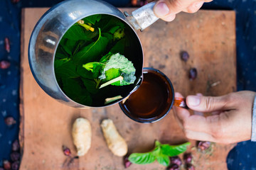 Woman hands pours herbal mint tea with ginger from pot into glass. Morning light and breakfast. Natural hot warning refreshing tea boiled with rose hip dried berries. Carrier of vitamins and health
