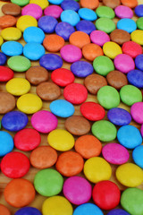 Shiny sugar coated round chocolate candies on light wooden background as multicolored textured sweet background.