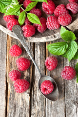 Fresh raspberries with leaves on rustic wooden background, top view