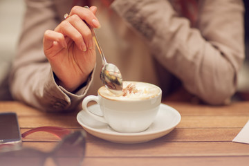 Fototapeta na wymiar young woman's hand holding a spoon, stir a cup of coffee in a street cafe on a wooden table, can be used as background