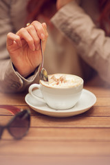 young woman's hand holding a spoon, stir a cup of coffee in a street cafe on a wooden table, can be used as background