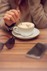 young woman's hand holding a spoon, stir a cup of coffee in a street cafe on a wooden table, can be used as background - 209909784