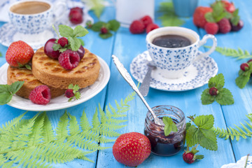 Delicious summer breakfast, homemade pastries and fragrant coffee. On a blue wooden background, berries and green leaves. Copy sapce.
