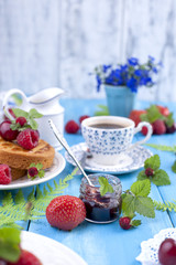 Delicious summer breakfast, homemade pastries and fragrant coffee. On a blue wooden background, berries and green leaves and flowers. Copy space