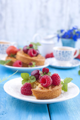 Delicious summer breakfast, homemade pastries and fragrant coffee. On a blue wooden background, berries and green leaves and flowers. Copy space.