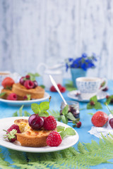 Delicious summer breakfast, homemade pastries and fragrant coffee. On a blue wooden background, berries and green leaves and flowers. Copy space