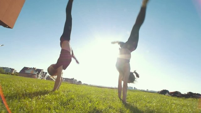 Young flexible women performing synchronous acrobatic wheel on the grass at sunny day