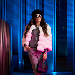 Full body portrait of young woman wearing round sunglasses, cap and white half-length fur coat...