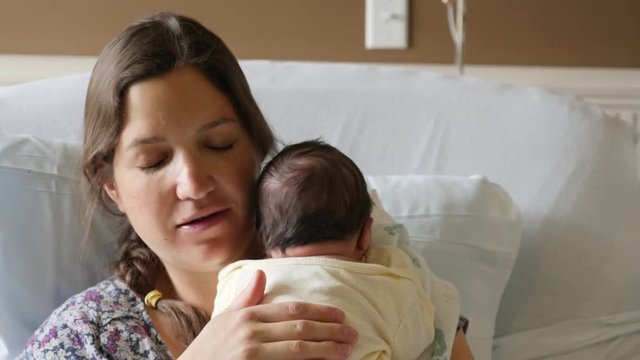 Tired mother burping a newborn girl after nursing her in the hospital