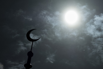 Silhouette of the Muslim crescent is a symbol of the Islamic religion towards the full moon or bright sun in the sky with clouds. For a stylish design of postcards or sacred celebrations.