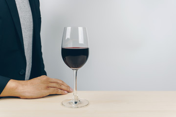 a glass of red wine on the wooden table, man in grey shirt and black suit in the background
