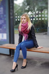A beautiful blonde girl is sitting at a public transport stop
