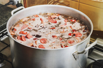 Cooking a big pan of Feijoada. Typical Brazilian cuisine, Feijoada has black beans, pork meat, bacon, sausage and spices. Cooking feijoada on a stove at home, homemade food.