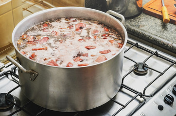 Cooking a big pan of Feijoada. Typical Brazilian cuisine, Feijoada has black beans, pork meat, bacon, sausage and spices. Cooking feijoada on a stove at home, homemade food.