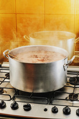 Cooking a big pan of Feijoada. Typical Brazilian cuisine, Feijoada has black beans, pork meat, bacon, sausage and spices. Cooking feijoada on a stove at home, homemade food.