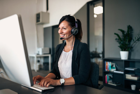 Beautiful customer representative with headset smiling during conversation with a client.