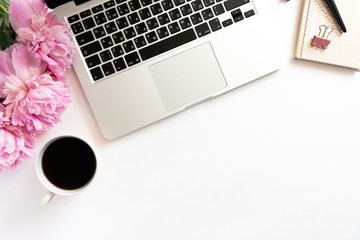 Home office desk with laptop, mug of coffee, golden notepad, bouquet of pink peonies on a white background