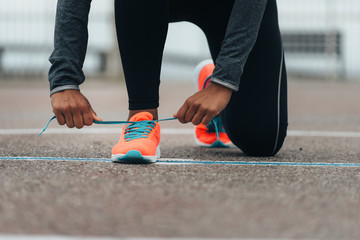 Detail of sporty swman lacing running shoes before before training. Outdoor city workout concept. Female fitness athlete getting ready for working out.