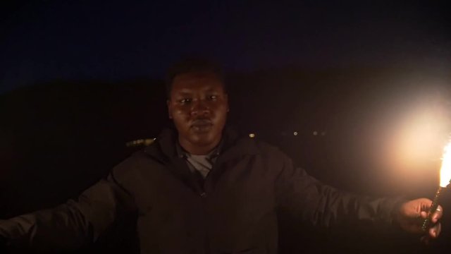 Young african man in nature with sparkler in hands at night