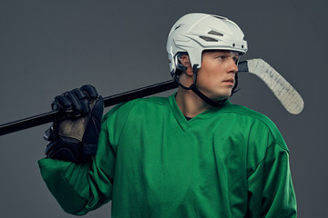 Professional hockey player in full equipment with gaming stick on shoulders against a gray...