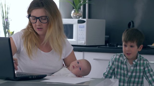 child interferes with the work of the business mom with a infant in her hands at kitchen