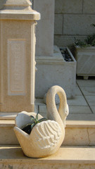 Statuette of white stone in the shape of a small swan on a background of a wall of a pot for scarlet.