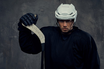 Hockey player wearing black protective gear and white helmet holds a hockey stick on a gray background.
