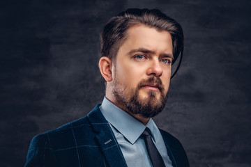 Close-up portrait of a handsome middle-aged man with beard and hairstyle dressed in an elegant formal suit. Isolated on a textured dark background in studio.