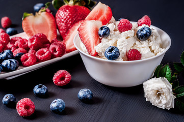 Cottage cheese with strawberries, blueberries and raspberries in a white plate on a black background with a white rose