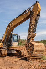 Orange excavator is on a backround of blue sky.