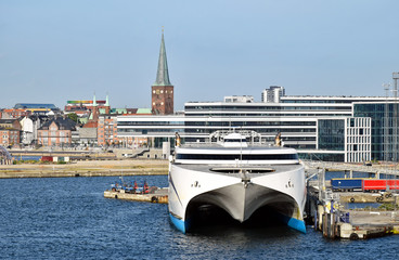 A high-speed ferry has moored in the harbor of Aarhus (Denmark). In the background modern and historic buildings can be seen. 