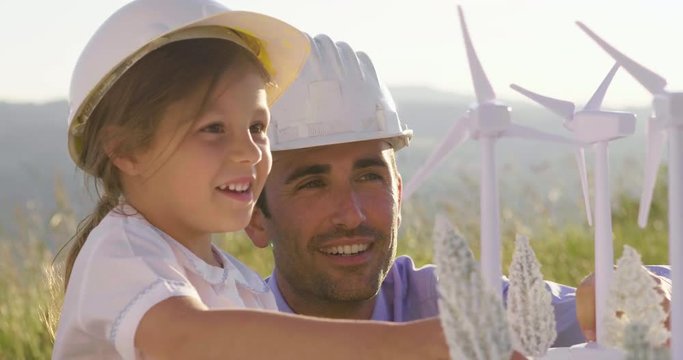A father engineer shows his project to his daughter for the construction of a wind farm. The daughter is interested in renewable energy. Concept of: family, engineering, future love for nature.