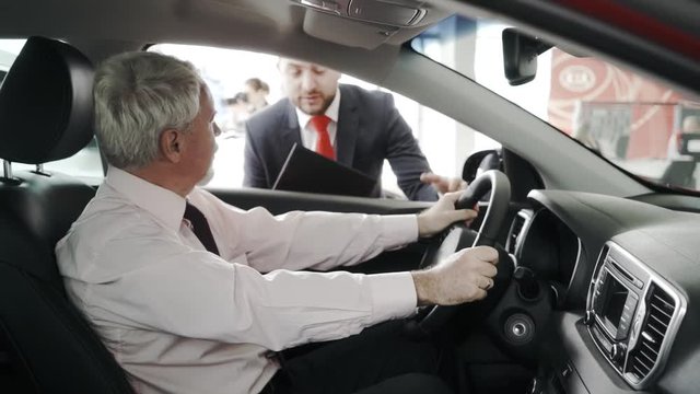 Test drive. Client at the steering wheel. The sales man is outside. Client closeup.