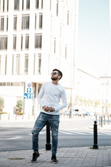 A young man travels through the streets of the city. Boy in sunglasses Stylish man near the building. The man sits on a whip. Beard and hair in a stylish guy.