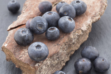 Blueberries in the foreground on tree bark and black slate background