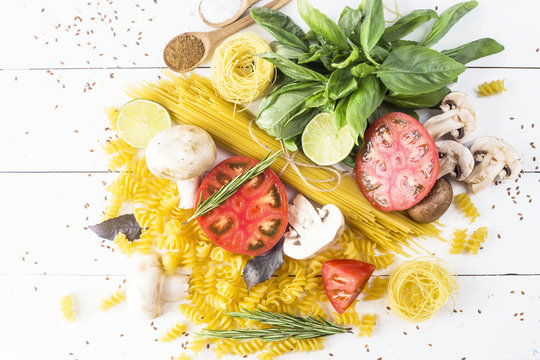 Food for cooking - pasta, basil, vegetables, lime and spices on a white wooden table in a heap. Top view, flat lay