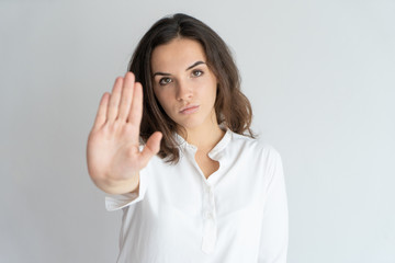 Serious determined girl showing stop sign. Young Caucasian woman in white blouse raising hand in no...