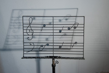 Metal artisan music stand with drawn musical notes, with a shadow of the staff of music