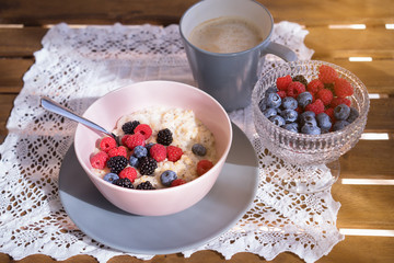Healthy breakfast - oatmeal with fresh berries in a bowl with a cup of coffee