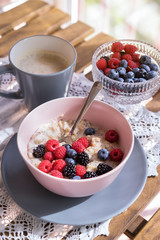 Healthy breakfast - oatmeal with fresh berries in a bowl with a cup of coffee