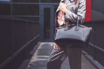 Trendy woman in silver pants jacket with black bag in hand street look. Fashionable outfit